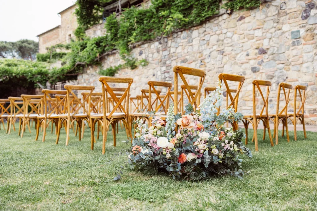 Sillas de ceremonia y decoración floral junto a un muro de piedra